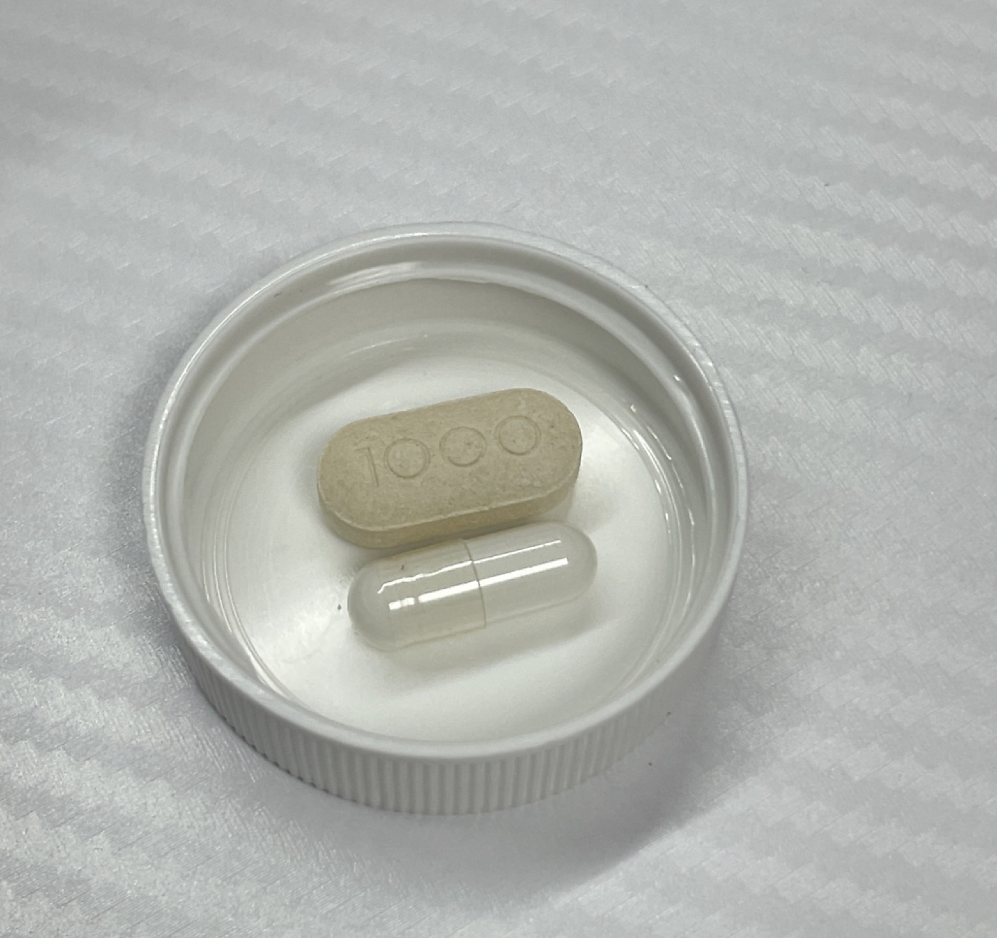 Thorne Glutathione-SR capsule next to a 1000mg vitamin C tablet for size comparison